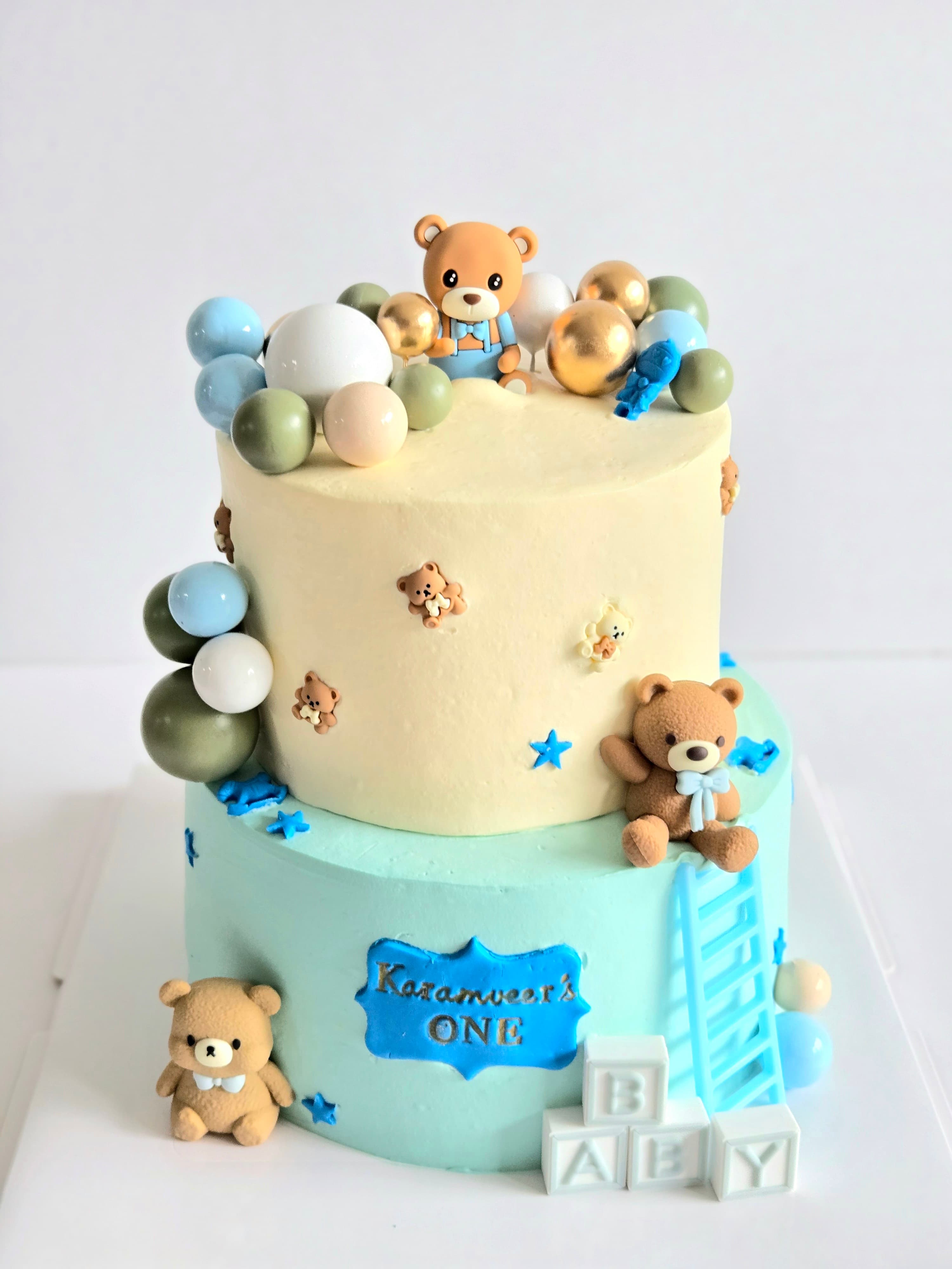 Two-tier teddy bear first birthday cake in cream and light blue
